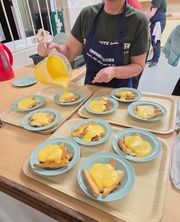 Kitchen team pour custard into bowls on trays of desserts