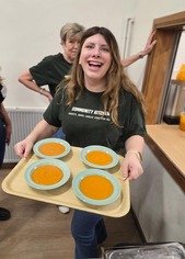 Woman with long hair carries a tray of four bowls of soup